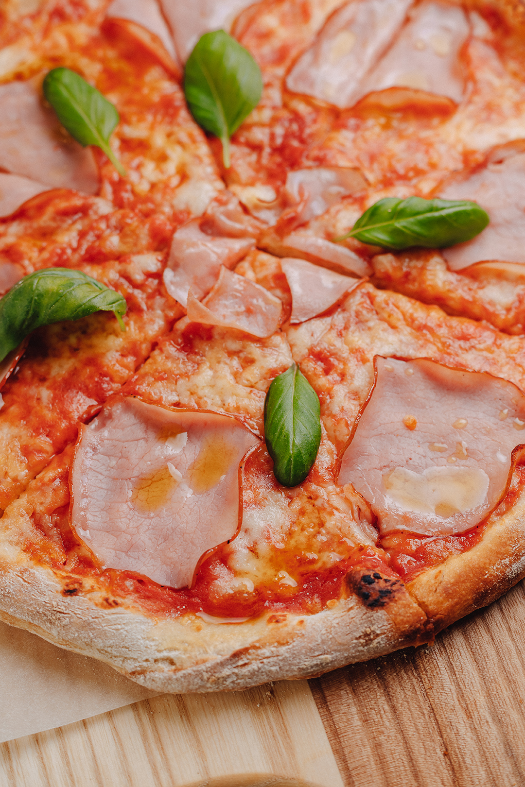 Neapolitan pizza on a cream sauce with ham, cheese, arugula, basil, tomatoes sprinkled with cheese on a wooden board on a tablecloth in a cell with a place for text